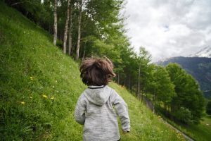 view from behind of a small child running on a grassy hillside