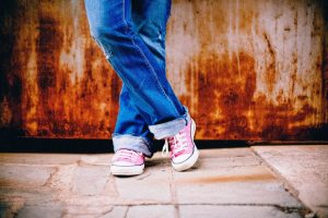 person from knees down, wearing blue jeans and pink converse all stars, standing in front of a rusting wall