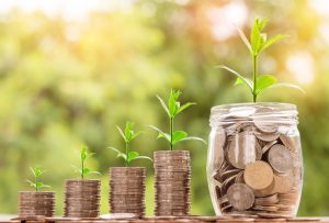 four increasingly large stacks of quarters with plants growing out of them, and a glass jar filled with coins and a plant growing out  of it