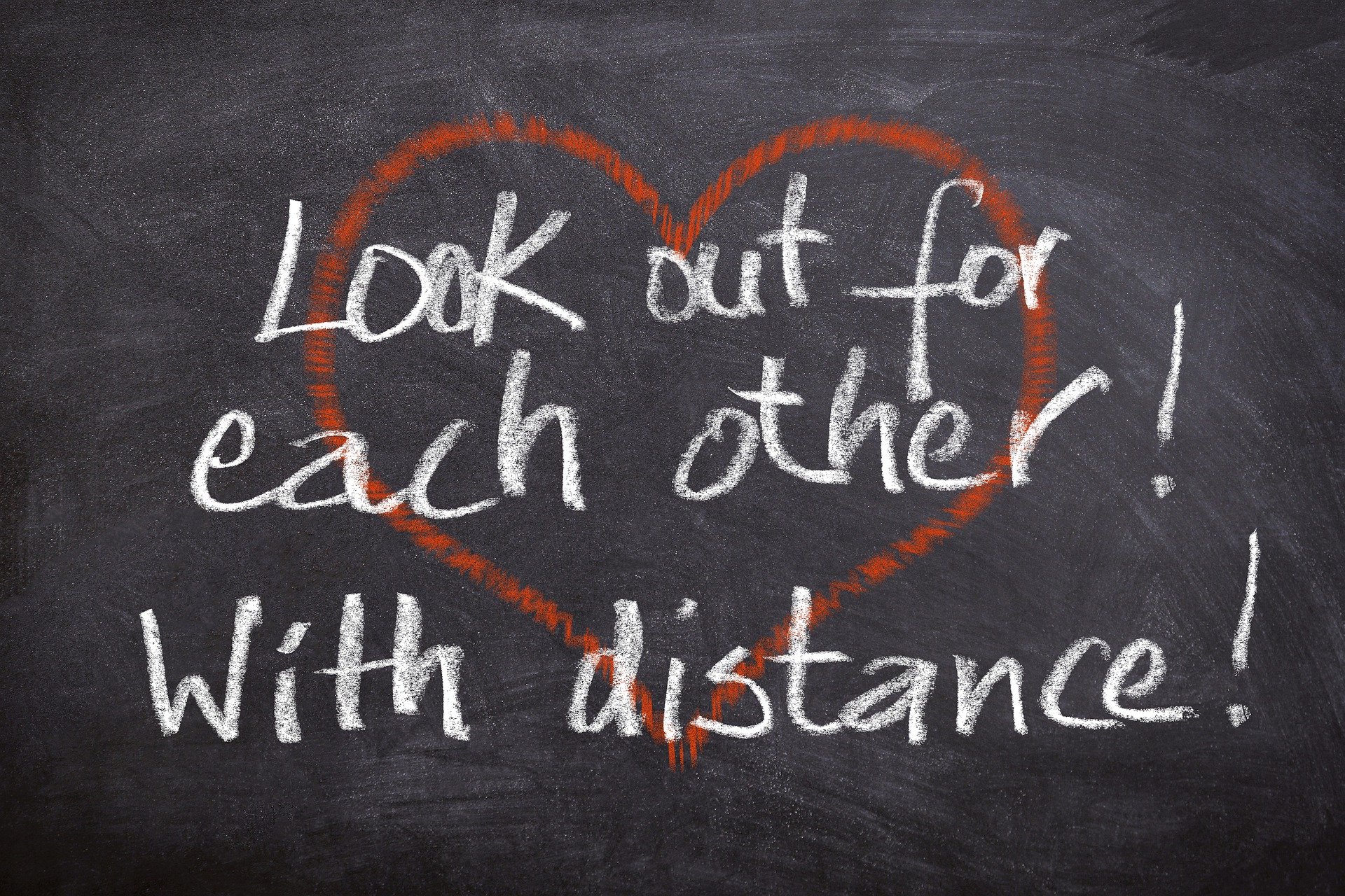 On a blackboard, a red heart and the words: Look out for each other! With distance!