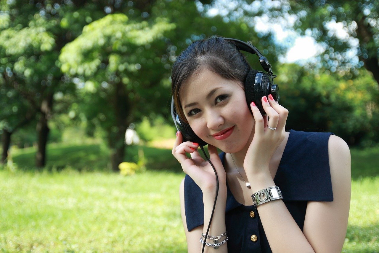 A teen sits outside on a summer day with earphones on