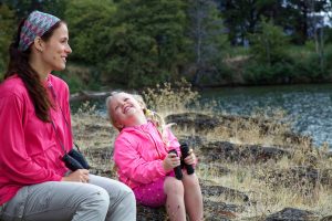 Adult woman sitting on bench with a child who is holding binoculars, looking at each other and laughing