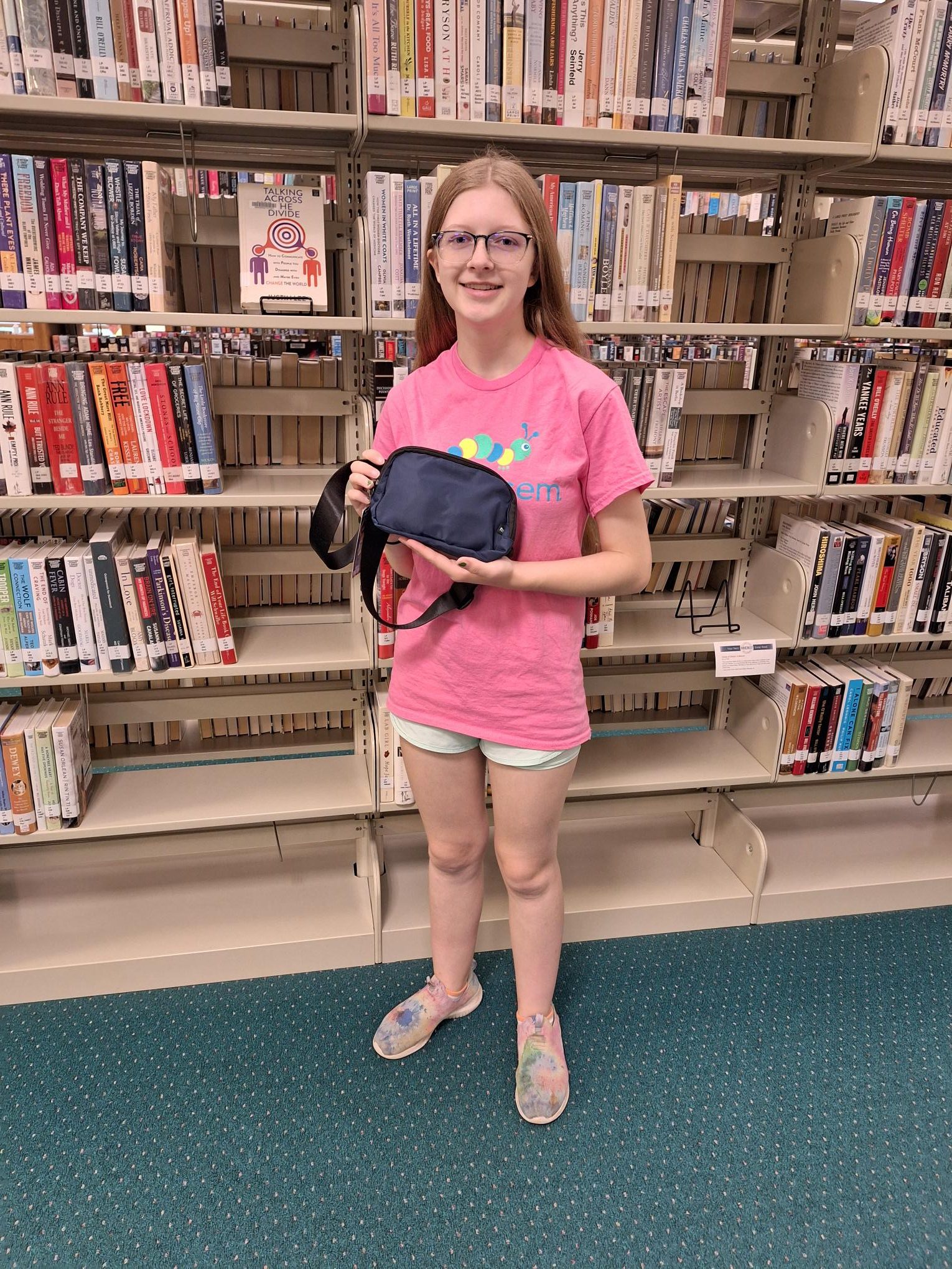teen in front of bookshelf holding waist pack prize