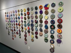 Colorful wall hanging consisting of CD's covered with yarn weaving and hung together.